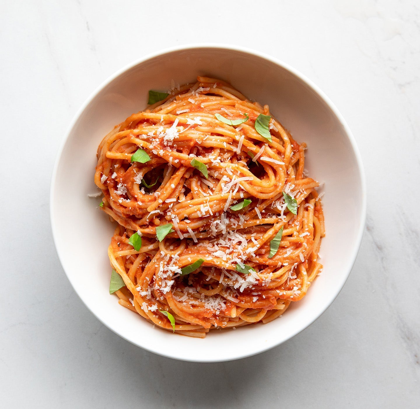 Prepared spaghetti tossed in tomato sauce with fresh herbs in a white bowl on a white background