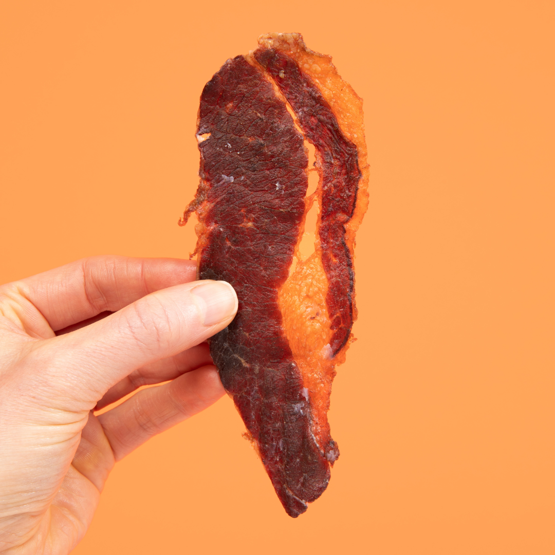 Hand holding a piece of dried meat against an orange background